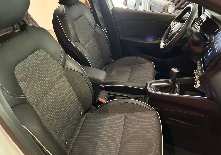 Vue intérieure côté conducteur de la Renault Clio V 1.0 TCE 90 Intens avec sièges tissu noir et coutures blanches.