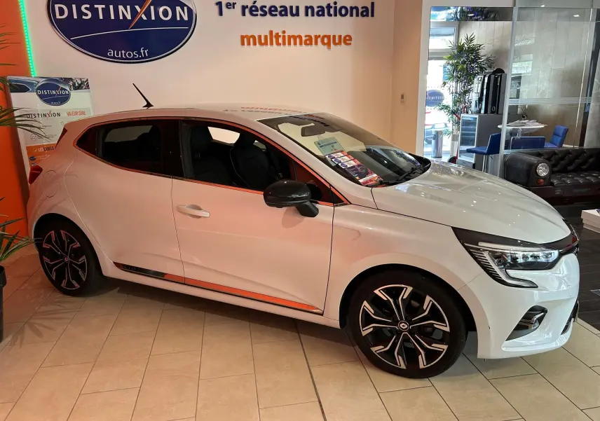Renault Clio V blanc nacré métal vue de profil côté droit en intérieur showroom avec jantes noires et détails chromés.