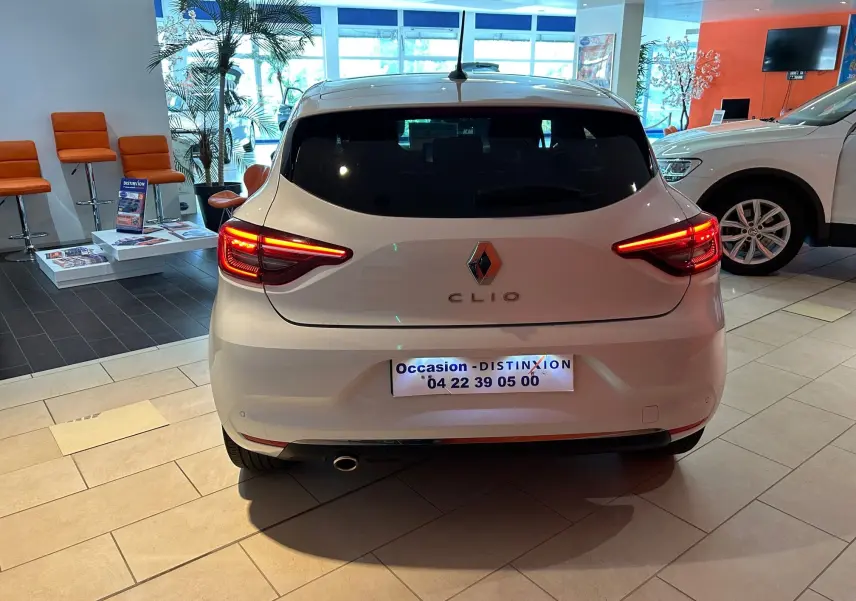 Vue arrière d'une Renault Clio V blanche nacrée, feux arrière allumés, en showroom lumineux.