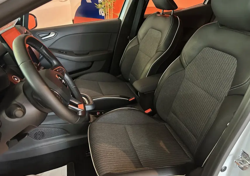 Intérieur de la Renault Clio V blanc nacré, vue côté conducteur montrant sièges tissu et cuir noir avec surpiqûres blanches.