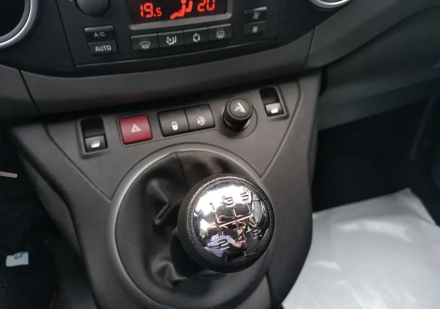 Gros plan sur le levier de vitesse manuel chromé du Peugeot Partner Tepee brun, avec tableau de bord et commandes visibles.