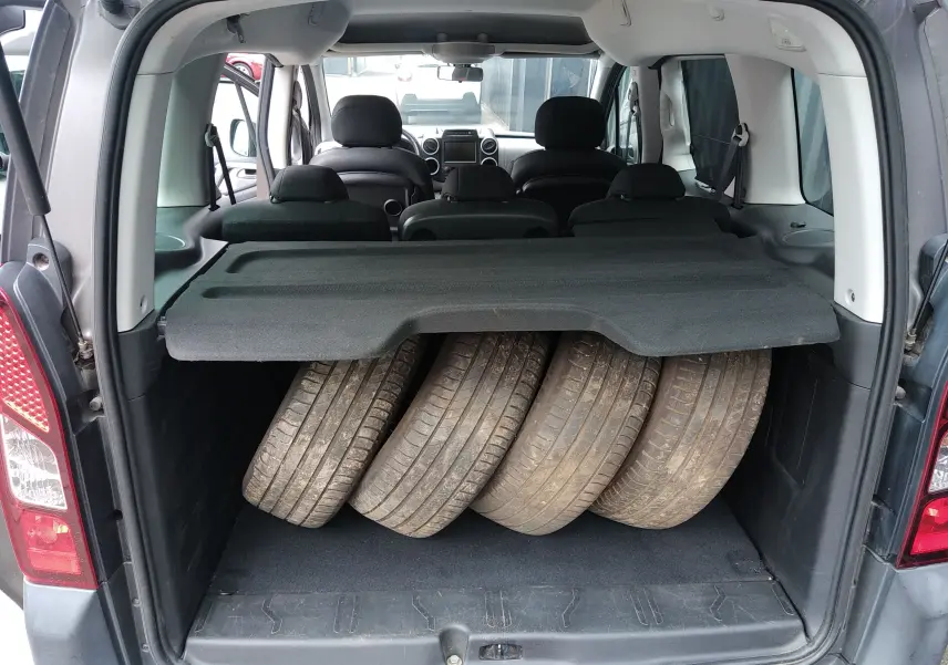 Vue arrière du Peugeot Partner Tepee brun 2017 avec coffre ouvert contenant quatre pneus usagés.