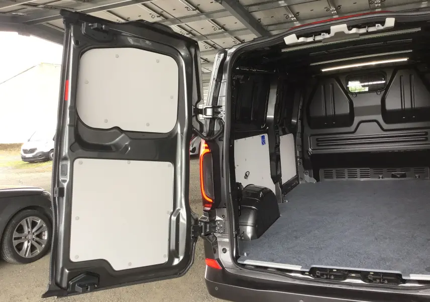Vue arrière ouverte du Volkswagen Transporter T7 gris anthracite, montrant l'espace de chargement vide et les panneaux intérieurs blancs des portes.