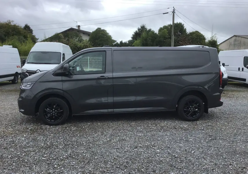 Profil côté gauche d'un Volkswagen Transporter T7 gris anthracite avec jantes noires sur un parking extérieur.