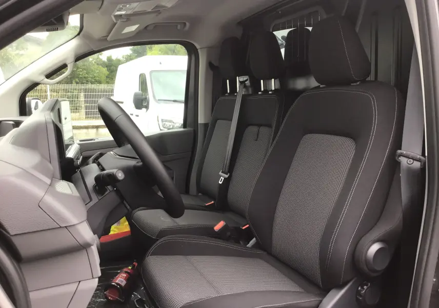 Intérieur du Volkswagen Transporter T7 2025, vue côté conducteur, sièges noirs avec appuie-têtes et séparation métallique arrière.