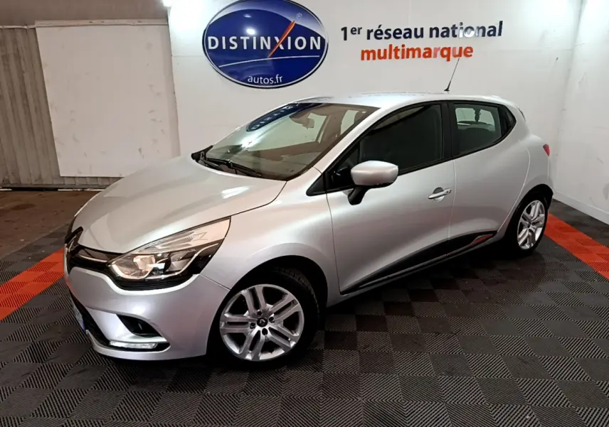 Renault Clio Business TCe 90 gris clair vue 3/4 avant droit dans un showroom avec logo Distinxion en arrière-plan