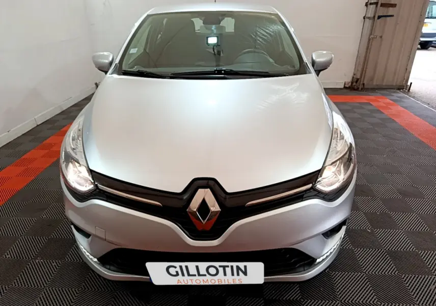 Renault Clio Business TCe 90 gris clair vue de face dans un garage avec phares allumés et logo Renault visible.