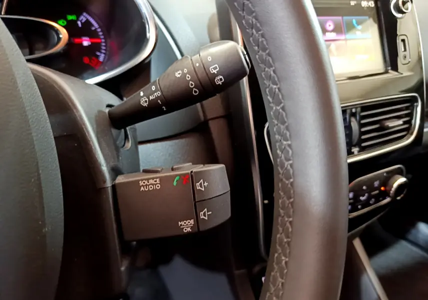 Gros plan sur le volant cuir et commandes audio au volant de la Renault Clio Business gris clair, avec écran tactile visible.