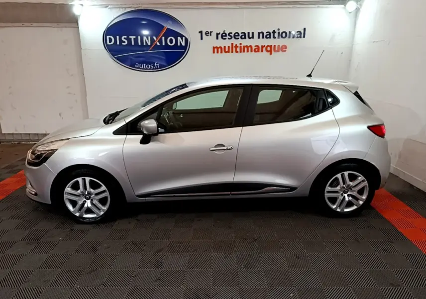 Profil côté gauche d'une Renault Clio Business TCe 90 gris clair, stationnée en intérieur sur sol noir et rouge.
