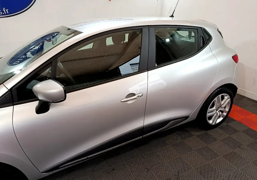 Profil côté gauche d'une Renault Clio Business TCe 90 gris clair, avec rétroviseur et poignées de porte visibles.