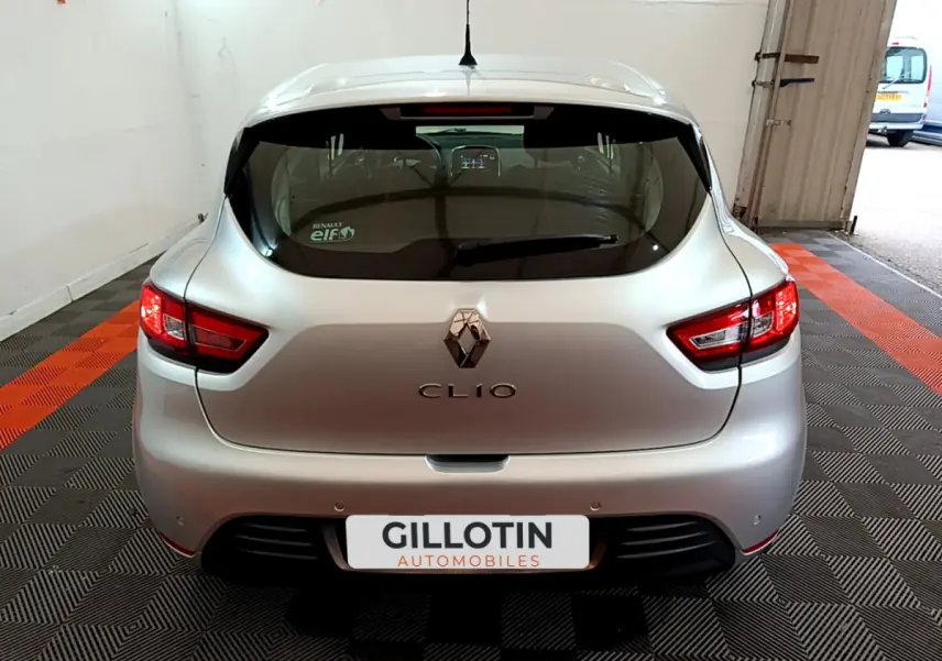 Vue arrière d'une Renault Clio gris clair 2019 avec feux arrière allumés et logo visible sur un sol à damiers noir et orange.
