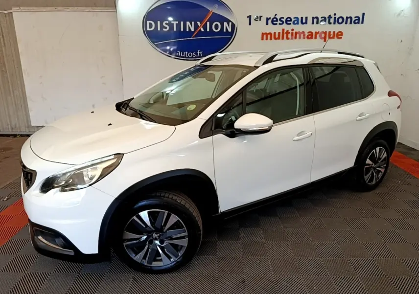 Peugeot 2008 blanc vue 3/4 avant droit, avec jantes alliage et barres de toit chromées en intérieur showroom.