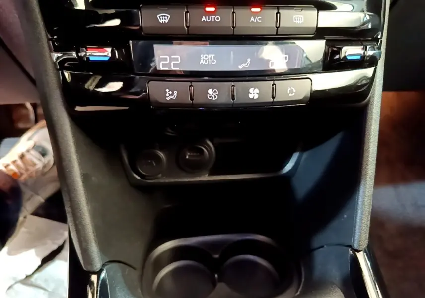 Gros plan sur la console centrale noire du Peugeot 2008 2019, montrant les commandes de climatisation digitale et les porte-gobelets.