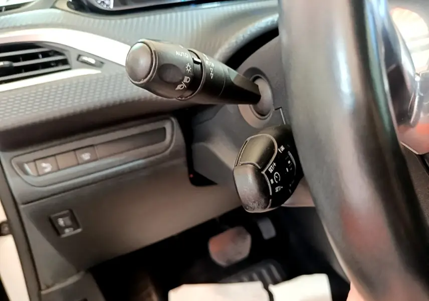 Gros plan sur la colonne de direction et commandes au volant noir du Peugeot 2008, intérieur sombre avec tableau de bord texturé.