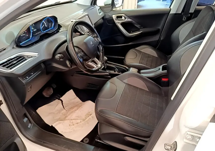 Vue intérieure côté conducteur de la Peugeot 2008 blanche, montrant sièges noirs et tableau de bord avec volant cuir.