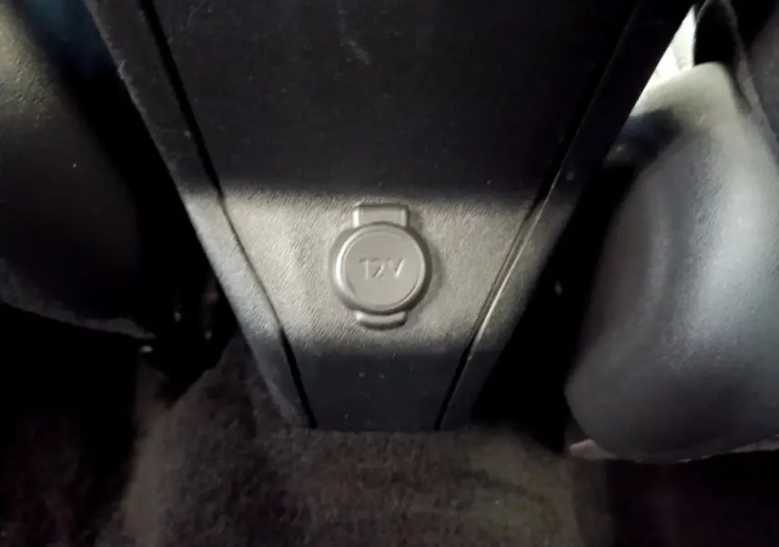 Prise 12V noire en gros plan au centre de la console arrière du Peugeot 2008 diesel, intérieur sombre.