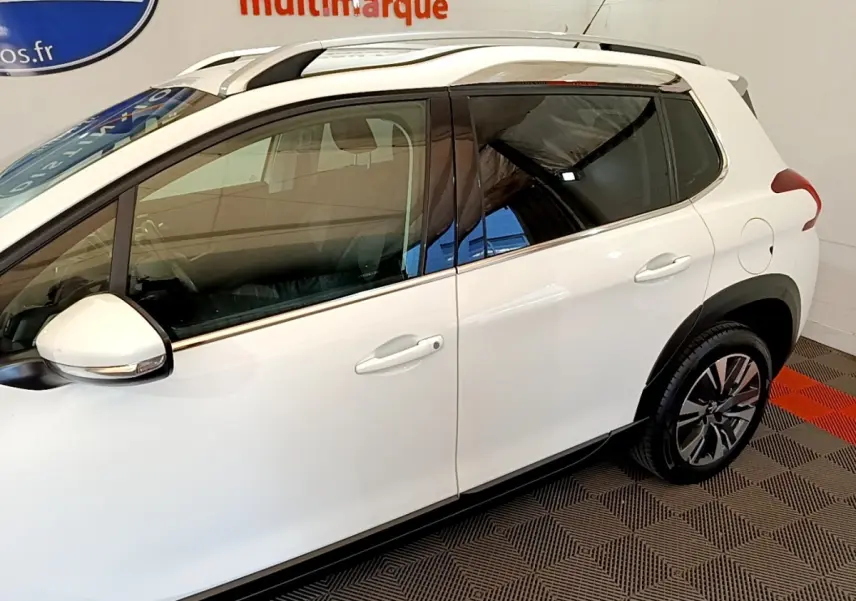 Vue côté droit du Peugeot 2008 blanc, mettant en valeur les jantes alliage et les barres de toit chromées.