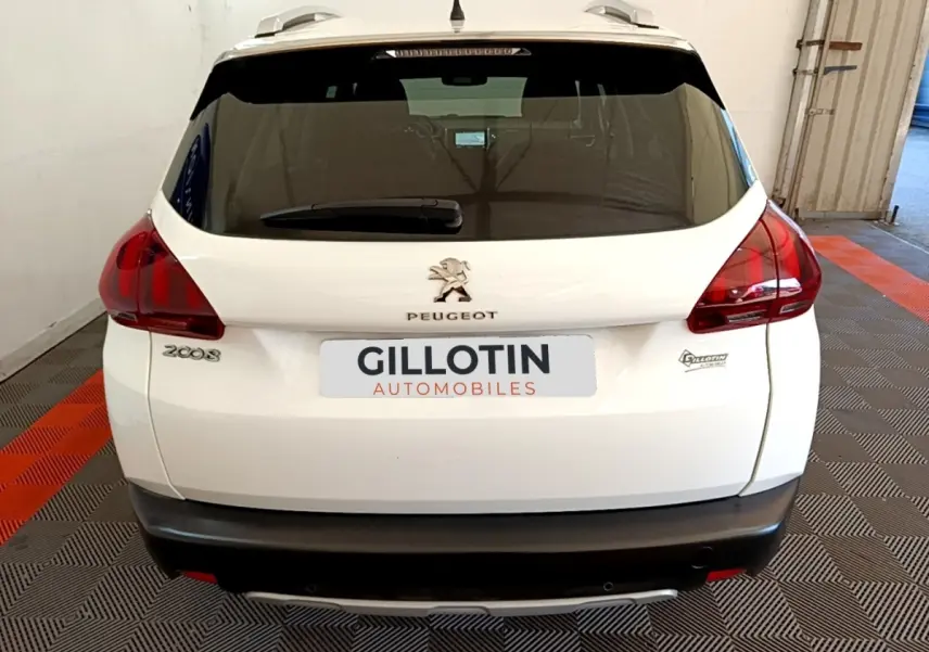 Vue arrière d'un Peugeot 2008 blanc avec feux arrière rouges et logo Peugeot visible sur un sol à damier noir et orange.
