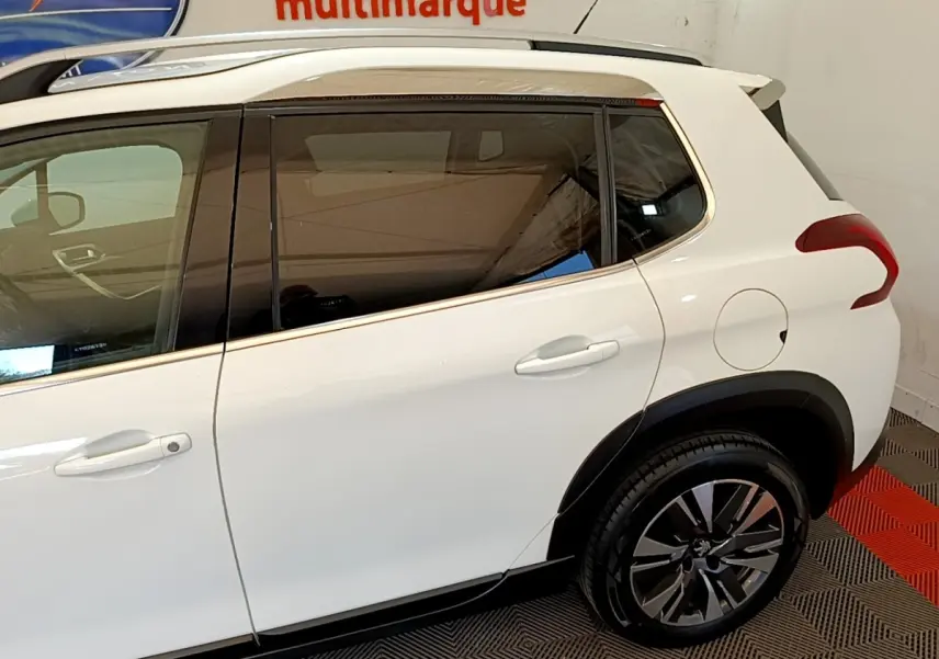 Vue côté gauche arrière du Peugeot 2008 blanc avec jantes alliage et vitres teintées en intérieur showroom.