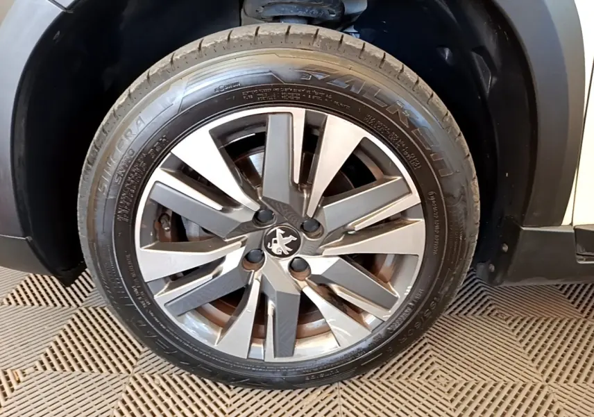 Gros plan sur la roue galette acier grise avec logo Peugeot, côté avant droit du véhicule blanc.