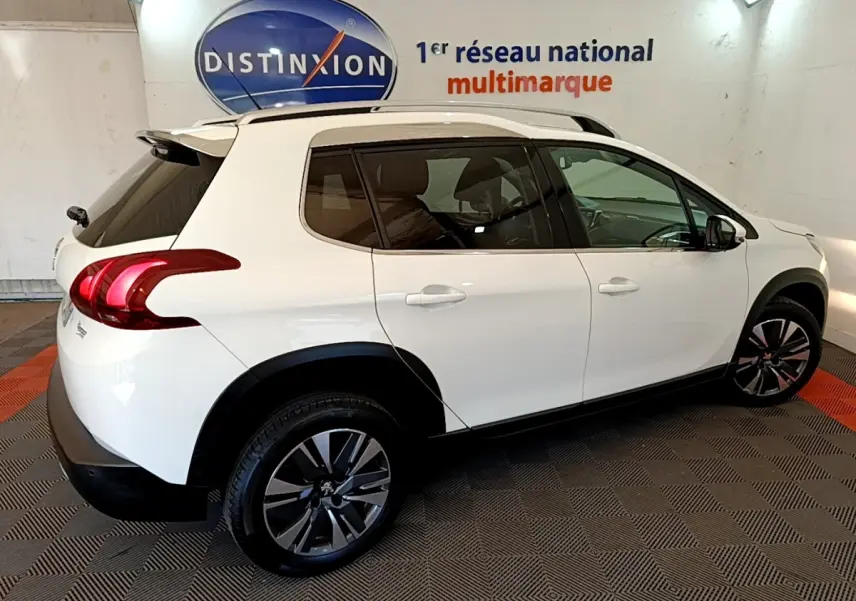 Peugeot 2008 blanc vue de profil droit en intérieur, avec jantes alliage et barres de toit chromées.