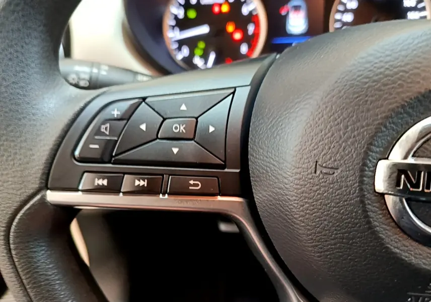Gros plan sur le côté gauche du volant noir de la Nissan Micra 2022 avec commandes multifonctions et logo Nissan visible.