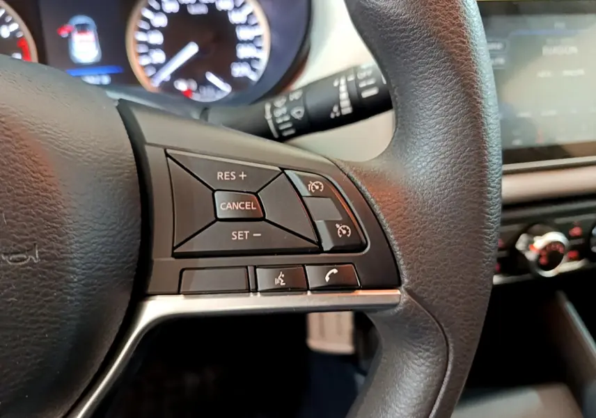 Gros plan sur les commandes du volant à droite dans l'habitacle d'une Nissan Micra blanche 2022, avec tableau de bord flou.