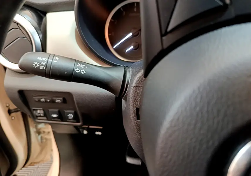 Gros plan sur le commodo gauche et le tableau de bord noir du Nissan Micra blanc, version IG-T 92 Acenta 2022.