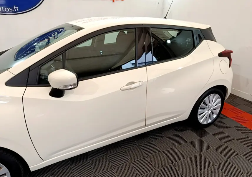 Profil côté gauche d'une Nissan Micra IG-T 92 Acenta blanche, avec rétroviseur et jante visibles sur fond intérieur.