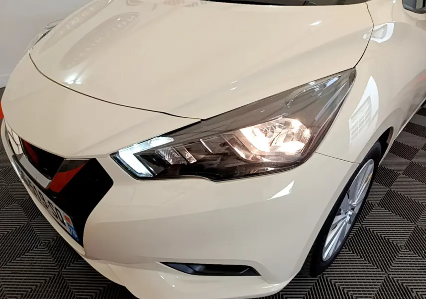 Vue 3/4 avant droit d'une Nissan Micra IG-T 92 Acenta blanche avec phares LED allumés et calandre noire distinctive.