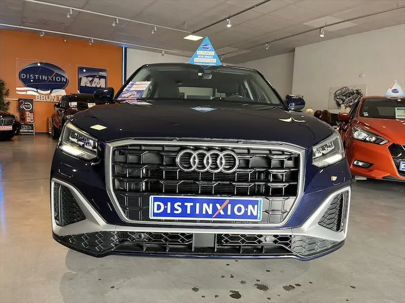 Vue frontale d'un Audi Q2 30 TFSI S-Line bleu Navarre métal avec calandre noire et logo Distinxion en concession.