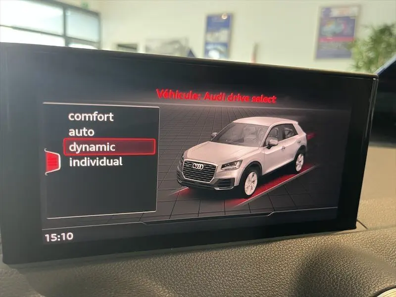 Affichage intérieur du système Audi drive select montrant un SUV Q2 blanc en 3/4 avant avec mode dynamique sélectionné.