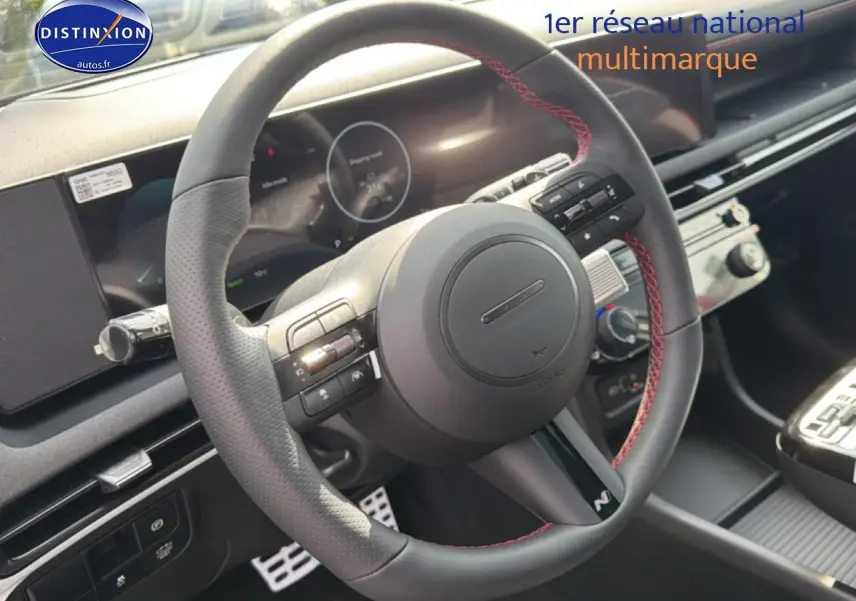 Vue rapprochée du volant cuir noir avec surpiqûres rouges du Hyundai Tucson 2026, tableau de bord et écran tactile visibles.