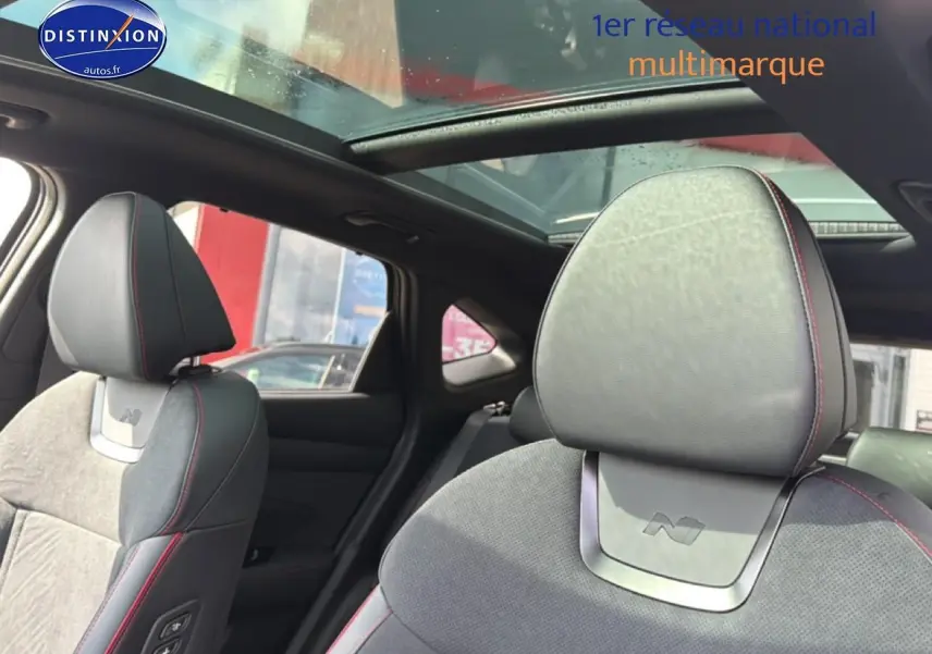 Détail intérieur montrant les sièges avant en cuir noir et alcantara avec surpiqûres rouges et toit panoramique en verre.