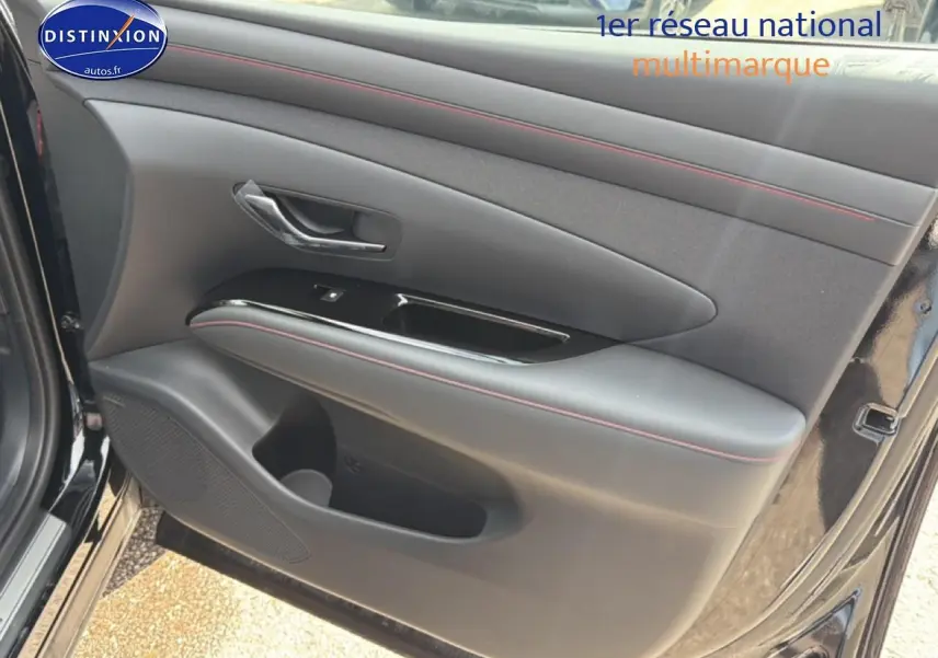 Vue rapprochée de la porte avant gauche noire du Hyundai Tucson 2026 avec surpiqûres rouges et poignée chromée.
