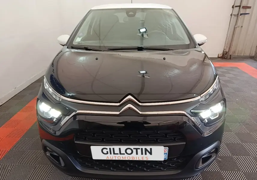 Vue avant d'une Citroën C3 noire avec toit blanc, phares LED allumés dans un garage.