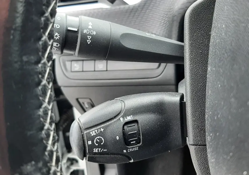 Gros plan sur les commandes de régulateur de vitesse et éclairage à gauche du volant d'un Peugeot 2008 blanc de 2017.