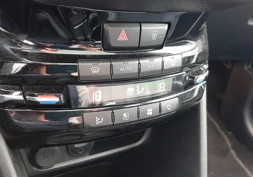 Gros plan sur la console centrale noire du Peugeot 2008 blanc de 2017, montrant les commandes de climatisation digitale.