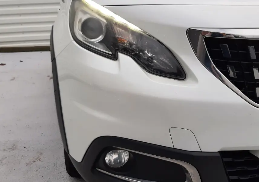 Gros plan sur l'avant gauche blanc d'un Peugeot 2008 2017, mettant en valeur le phare et le antibrouillard chromé.