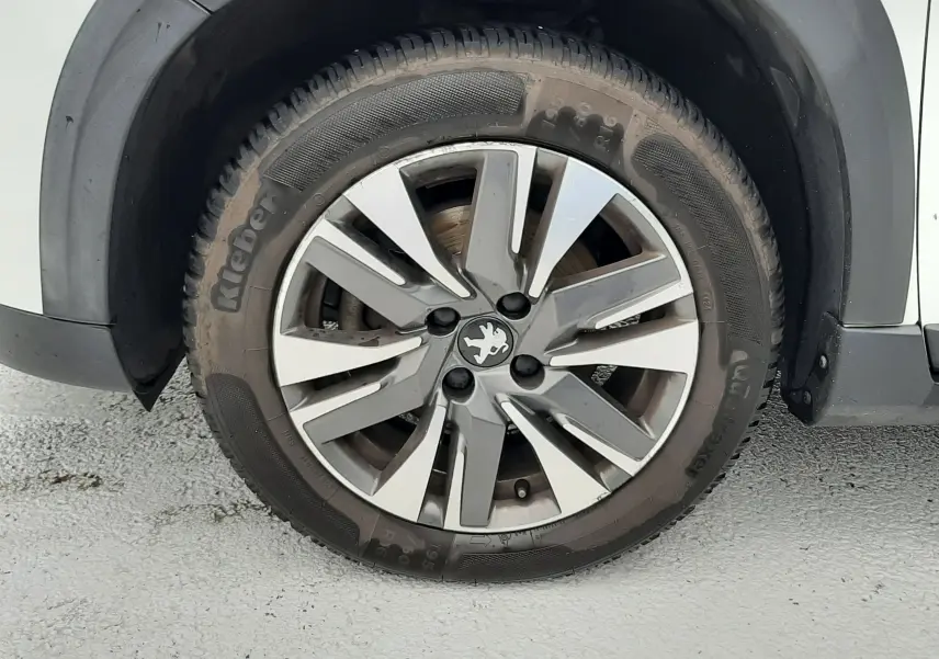 Gros plan sur la roue avant gauche d'un Peugeot 2008 blanc de 2017 avec jante alliage et logo lion central.