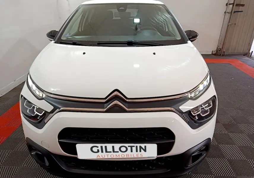 Vue frontale d'une Citroën C3 blanche 2023 avec phares LED et calandre noire distinctive en intérieur showroom.