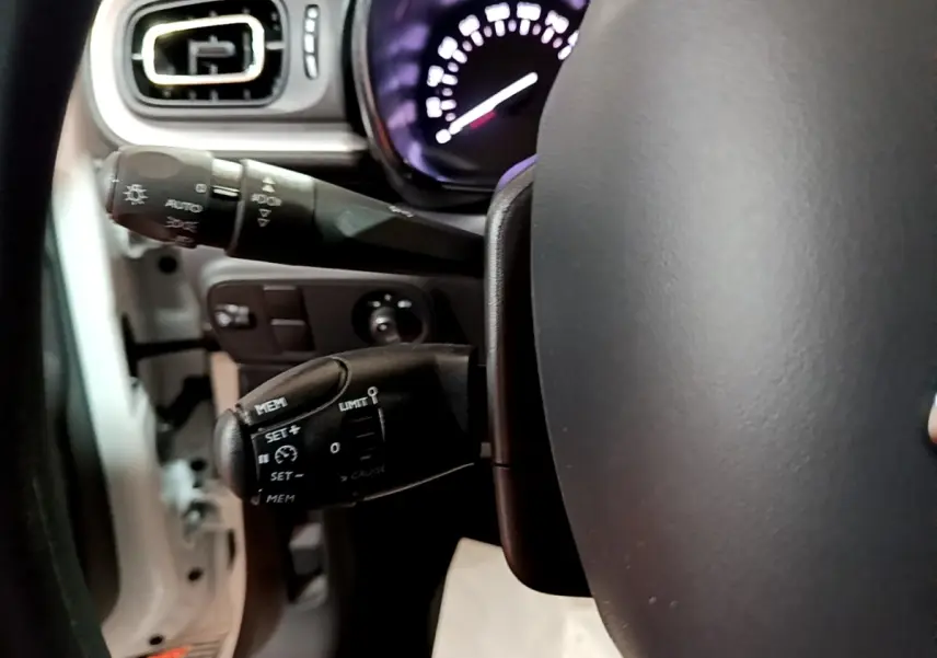 Gros plan sur la commande de régulateur de vitesse à gauche du volant dans l'habitacle d'une Citroën C3 blanche.