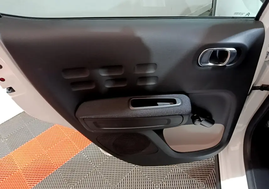 Porte intérieure côté gauche noire et grise de la Citroën C3 blanche 2023, avec poignée chromée et commande de vitre manuelle.