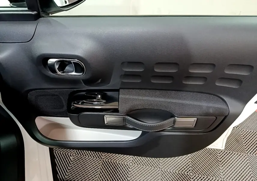 Détail de la porte côté conducteur noire et blanche de la Citroën C3 PureTech 83 Shine 2023 avec poignée et commandes intégrées.