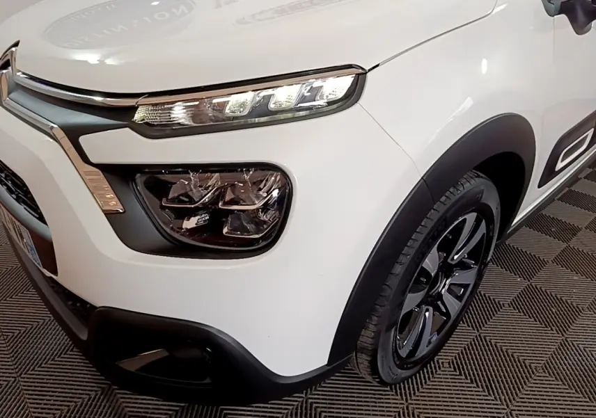 Vue 3/4 avant droit d'une Citroën C3 blanche 2023 avec phares LED et jantes noires distinctives.