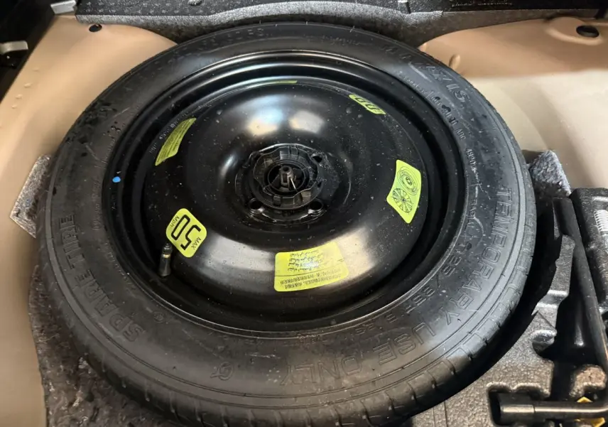 Gros plan sur la roue de secours noire dans le coffre d’une Peugeot 2008 orange, avec étiquettes jaunes visibles.