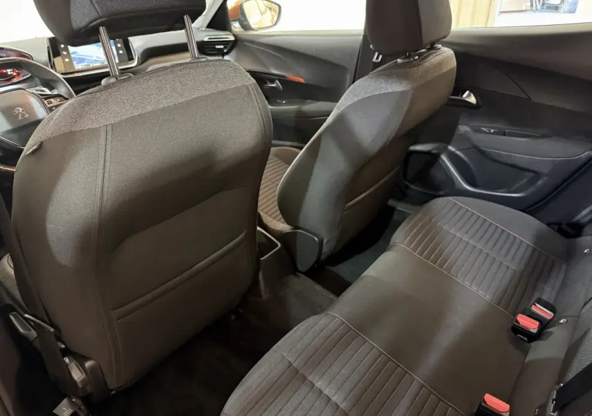 Vue intérieure arrière de la Peugeot 2008 2022, sièges tissu noirs avec surpiqûres rouges, tableau de bord et volant visibles.