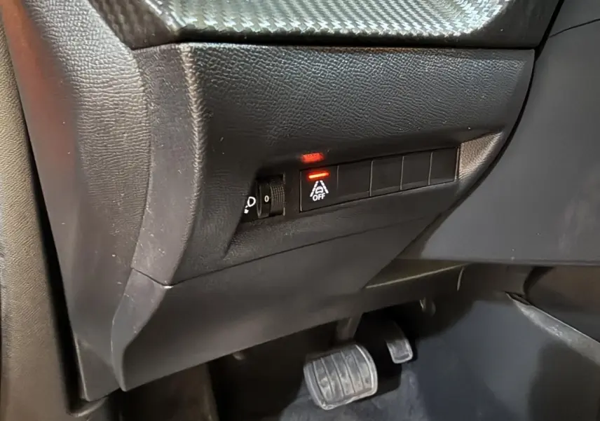Vue intérieure côté conducteur du tableau de bord noir avec bouton d'arrêt de l'assistance à la conduite allumé dans un Peugeot 2008 orange.