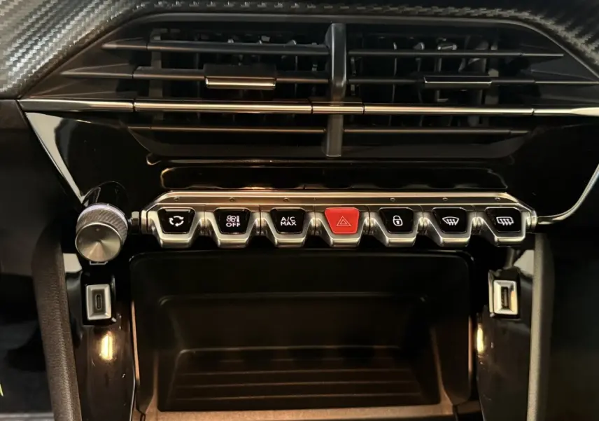 Vue rapprochée du tableau de bord noir brillant du Peugeot 2008 avec rangée de boutons métalliques et bouton rouge d’alerte.