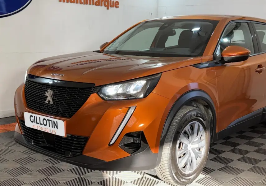 Vue 3/4 avant droit d’un Peugeot 2008 orange 2022 avec calandre noire et feux LED allumés en intérieur showroom.